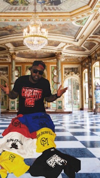 a man in a black t - shirt is posing in front of several t - shirts